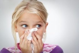 A girl sneezing onto a tissue.